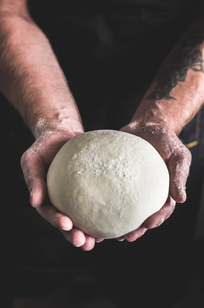 pizza chef_holding_a_pizza_dough_in_his_two_hands @Artur Rutkowski